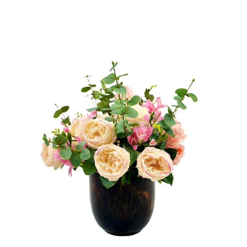 A mix of artificial roses eucalyptus and freezia in a tortoise shell glass vase.