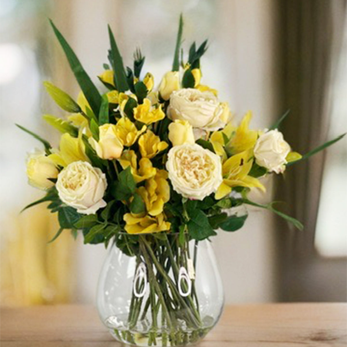 Bouquet of yellow and white faux flowers in a clear vase on a wooden surface.