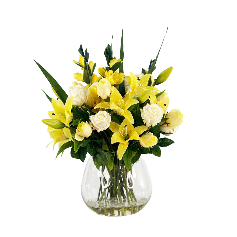 Arrangement of yellow and white faux flowers in a clear vase on a white background