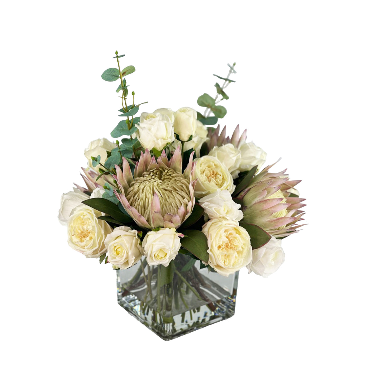 Bouquet of faux flowers with proteas and roses in a clear vase with faux water on a white background