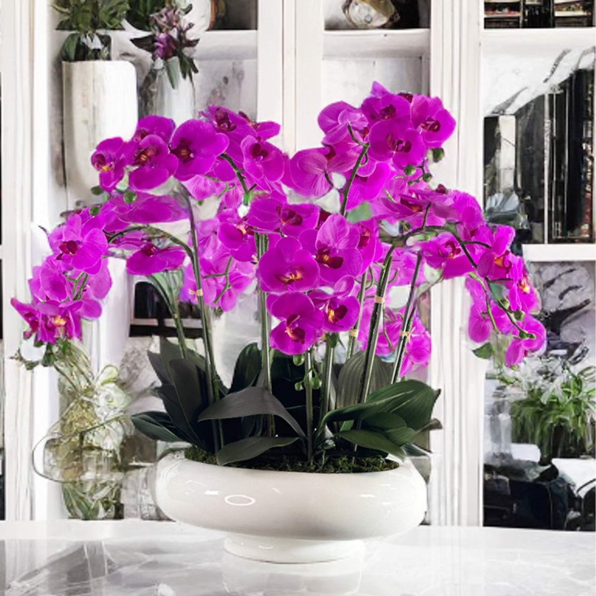 Purple oartificial Orchids in a white pot on a table with a blurred indoor background