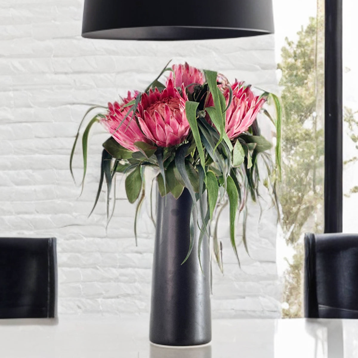 Vase with pink Faux Protea flowers with  eucaluptus on a table in a room with a window