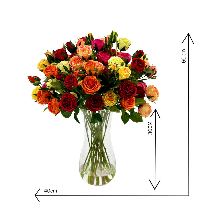 A waisted glass vase containing an arrangement of artificial mixed roses in various colors set in faux water with measurements