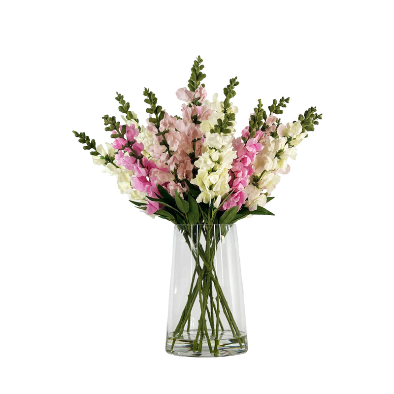 Bouquet of faux pink and white snapdragons in a clear glass vase with faux water on a white background