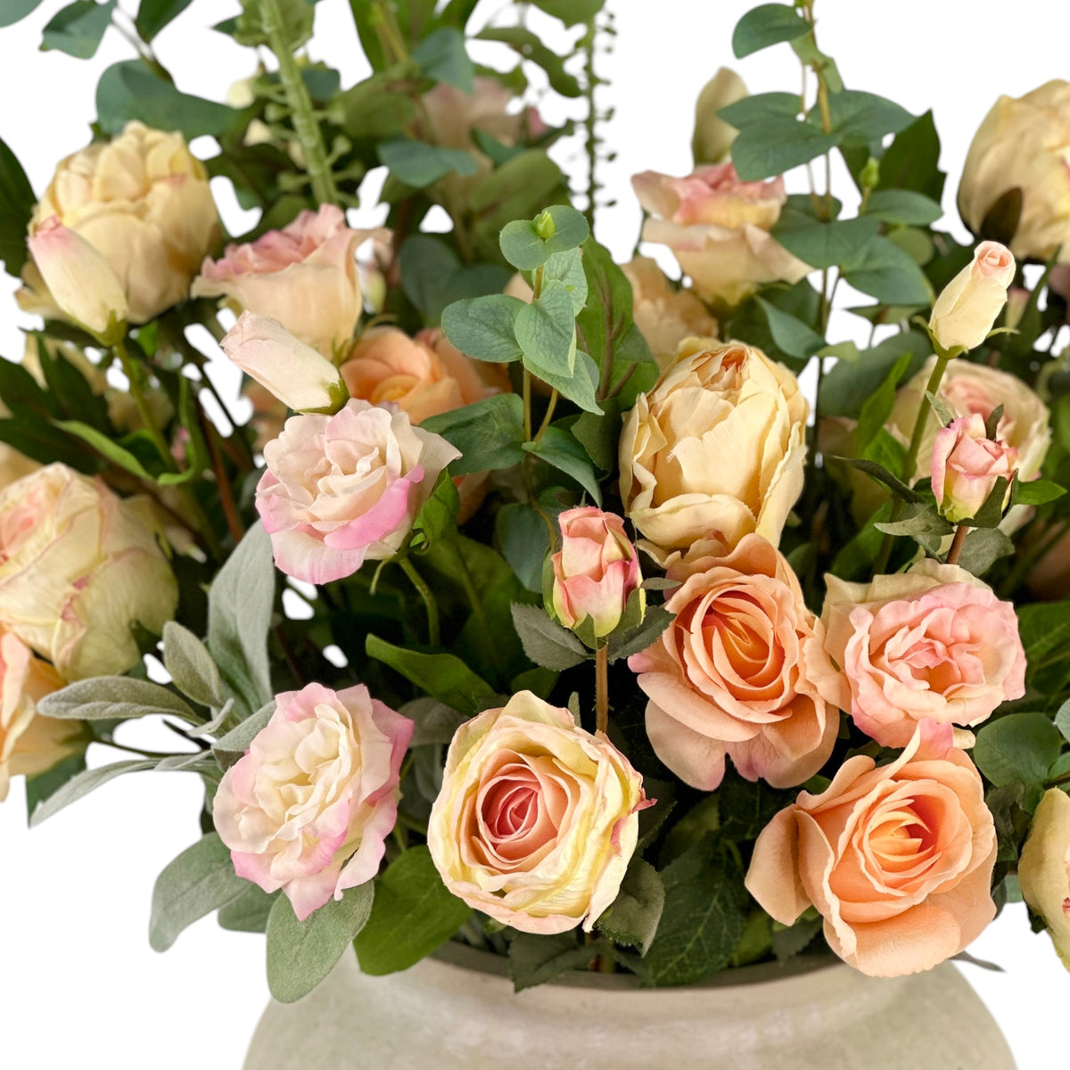 Close up of faux Bouquet of pastel-colored roses with green leaves in a white vase.