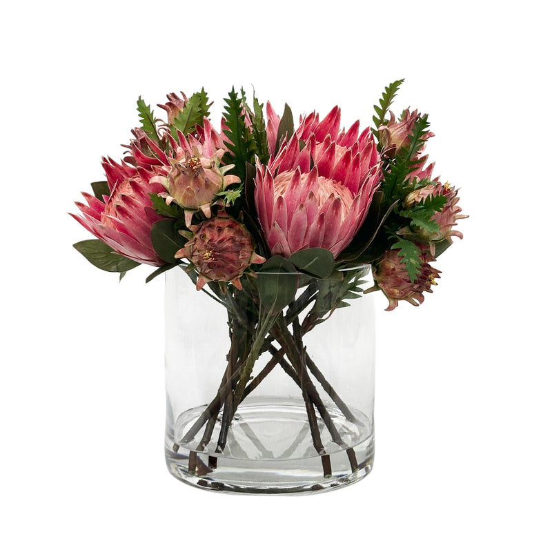 Bouquet of pink Faux protea flowers in a clear glass vase on a white background